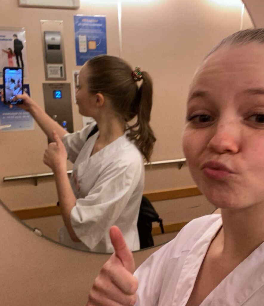 To personer i hvite uniformer tar en selfie i et heisspeil, og begge gir tommelen opp. Den ene er vendt mot kameraet, mens den andre er sett fra siden.