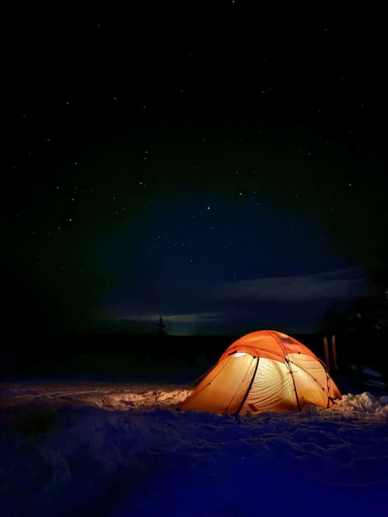 fff1c8b7-a39e-4d6f-b23b-dbf9fa762773 Et oransje telt lyser opp i et snødekt landskap om natten under en stjerneklar himmel.